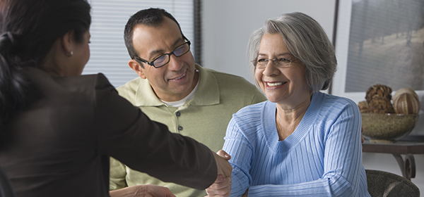Seated couple with female shaking hands with person sitting across the table